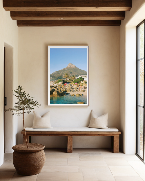 Framed artwork of a coastal scene on a wall above a wooden bench with a plant.