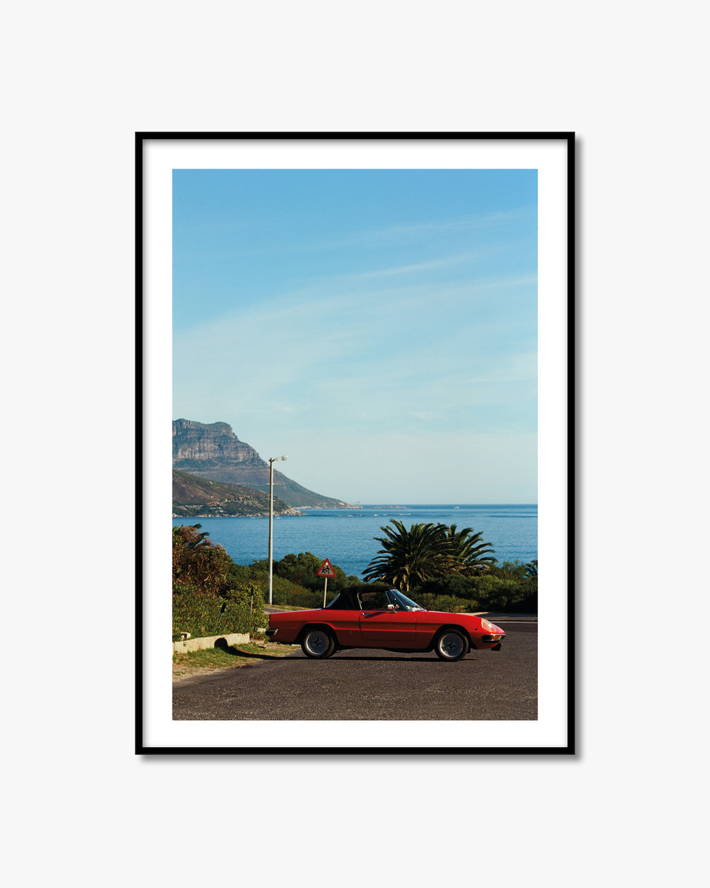 Framed artwork of a red car by the sea with mountains in the background