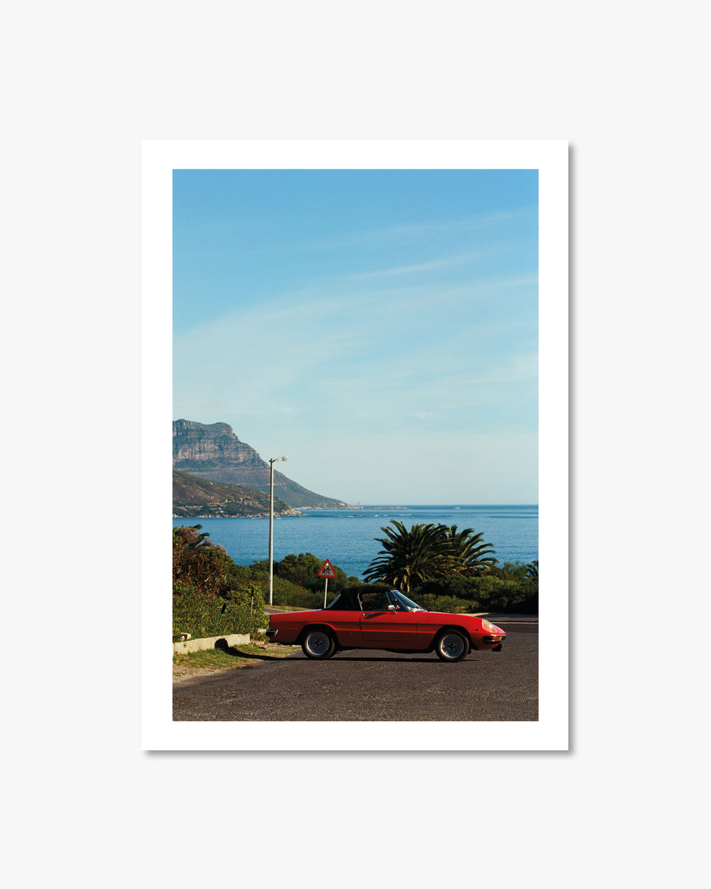 Red car parked on a scenic road with ocean and mountain view
