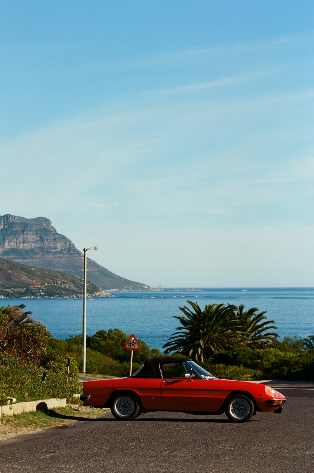 Red convertible car on a scenic road with mountains and ocean in the background