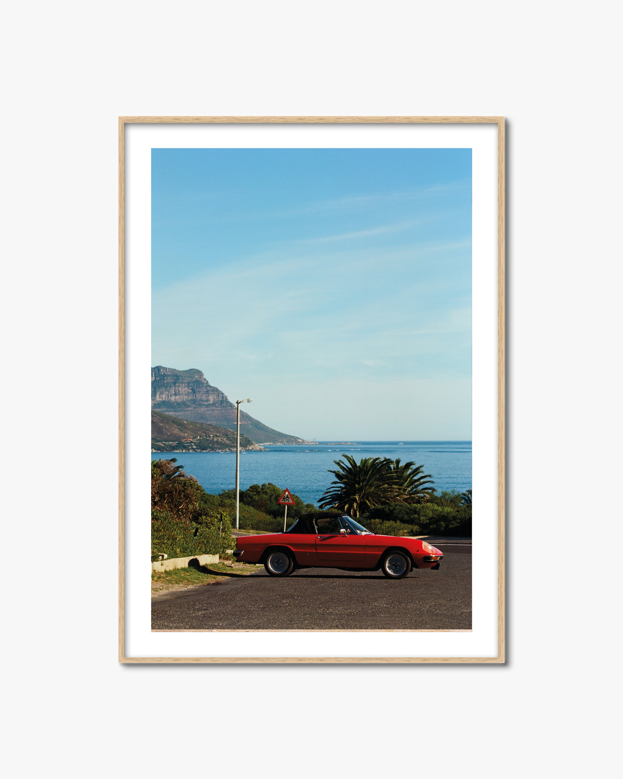 Framed artwork of a red car by the sea with Table Mountain in the background.