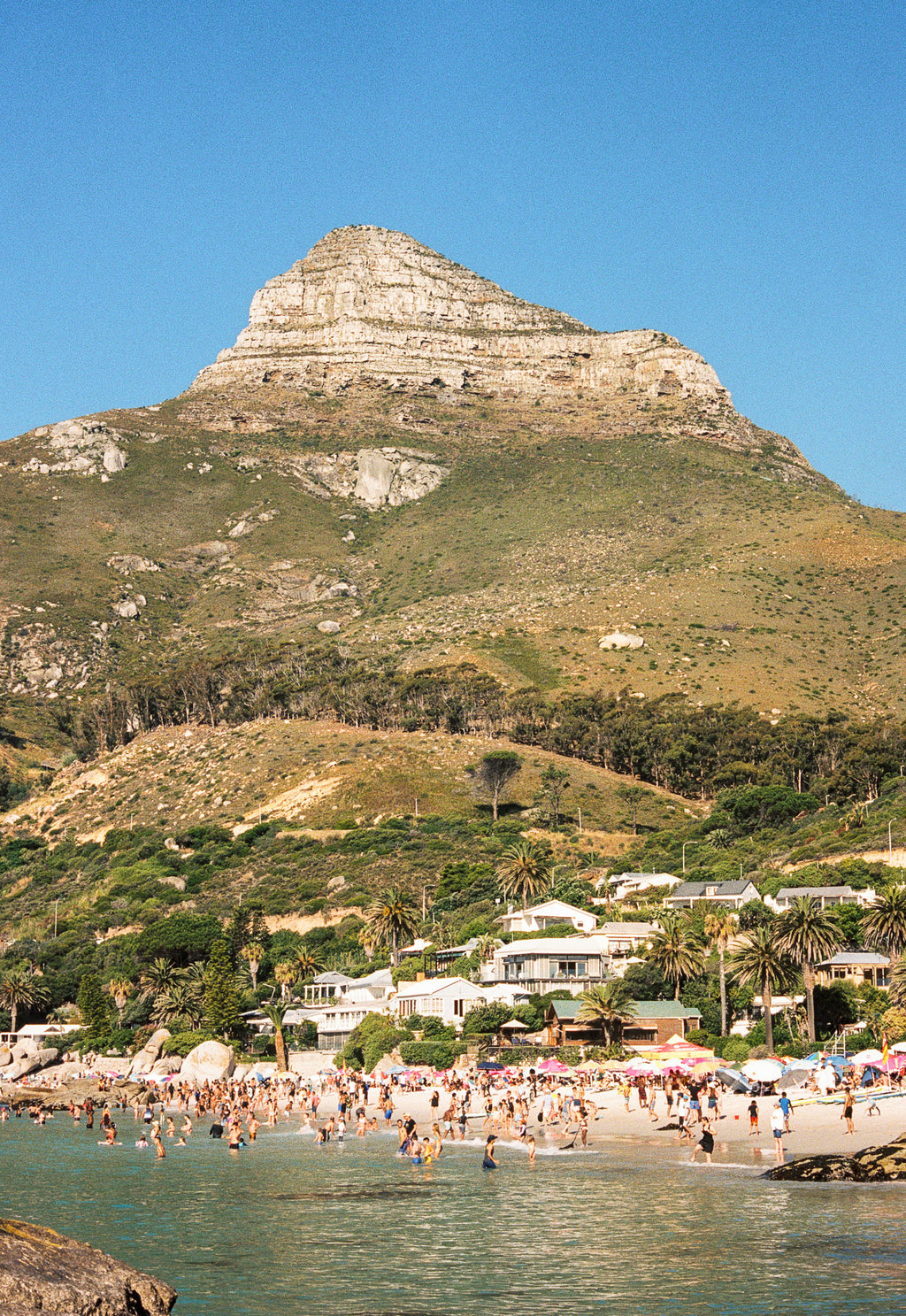 Beach scene with people enjoying the water, Lion's Head mountain in the background.