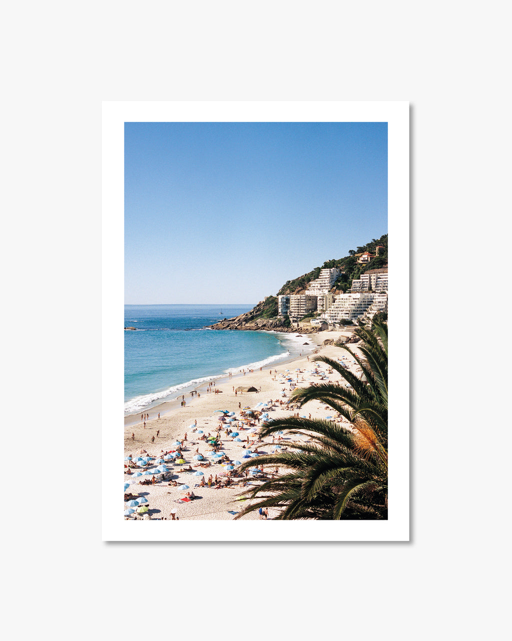 Beach scene with people, umbrellas, and palm trees with a clear blue sky.