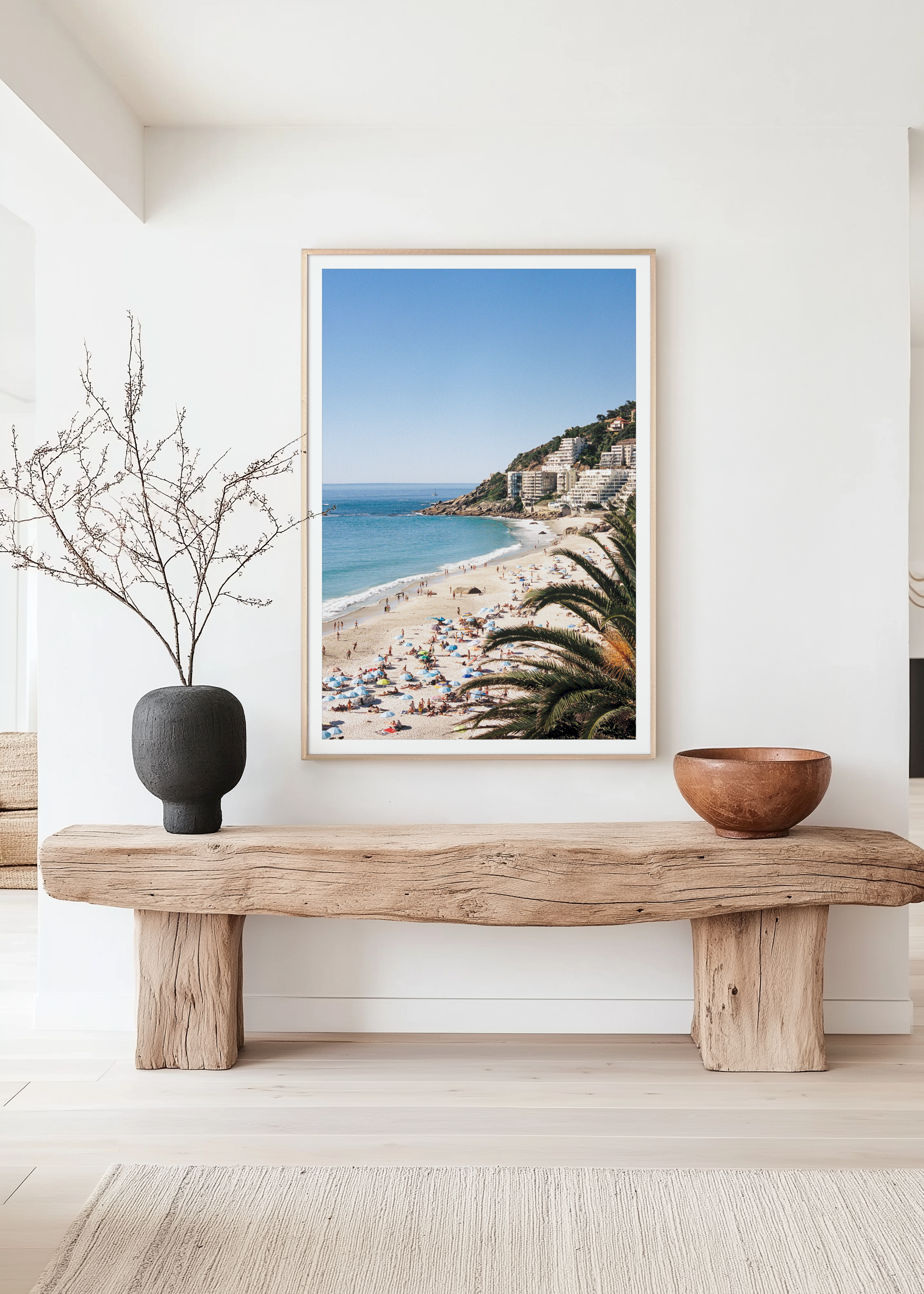 Framed beach scene print on a wall above a wooden bench with decorative items.