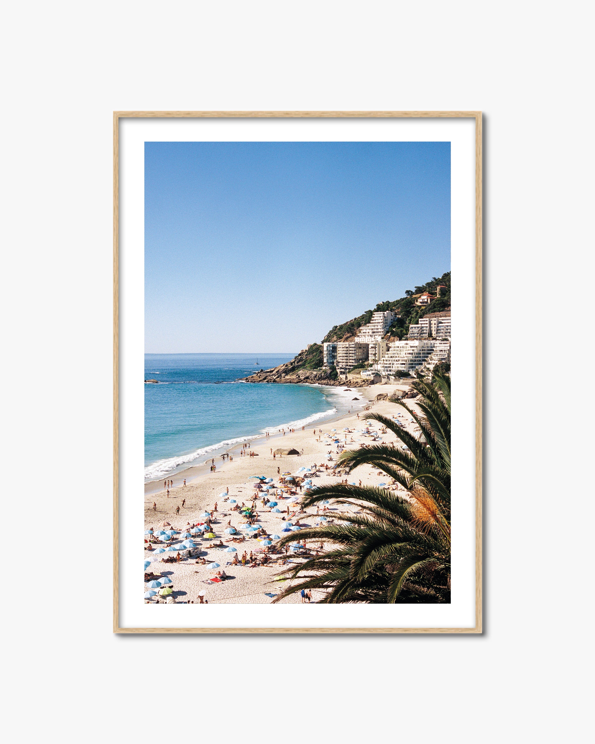 Framed photograph of a beach scene with people, umbrellas, and palm trees.