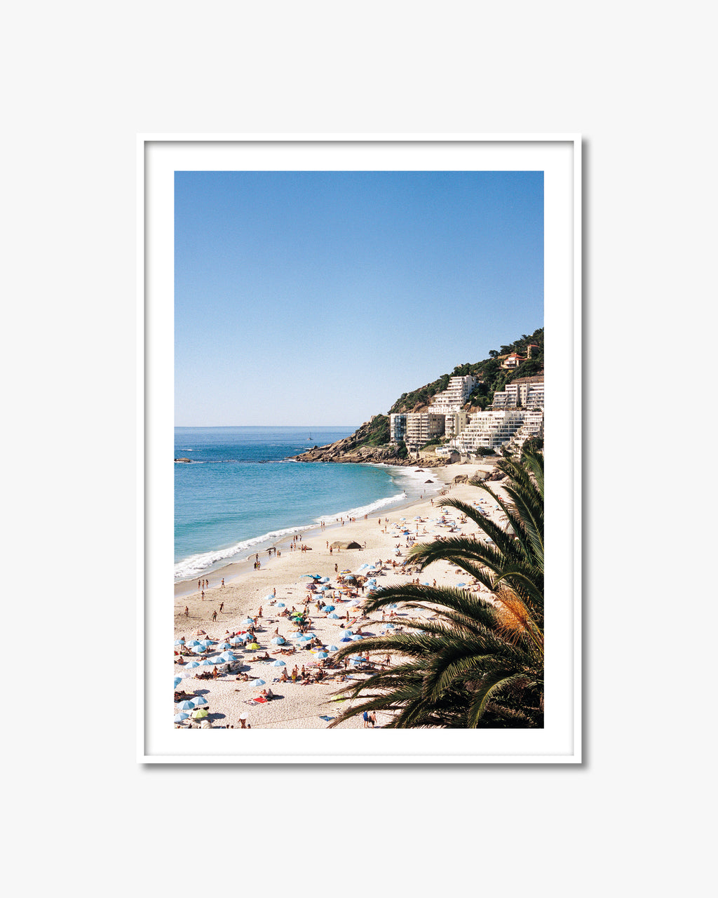 Framed photograph of a beach scene with people, umbrellas, and palm trees.