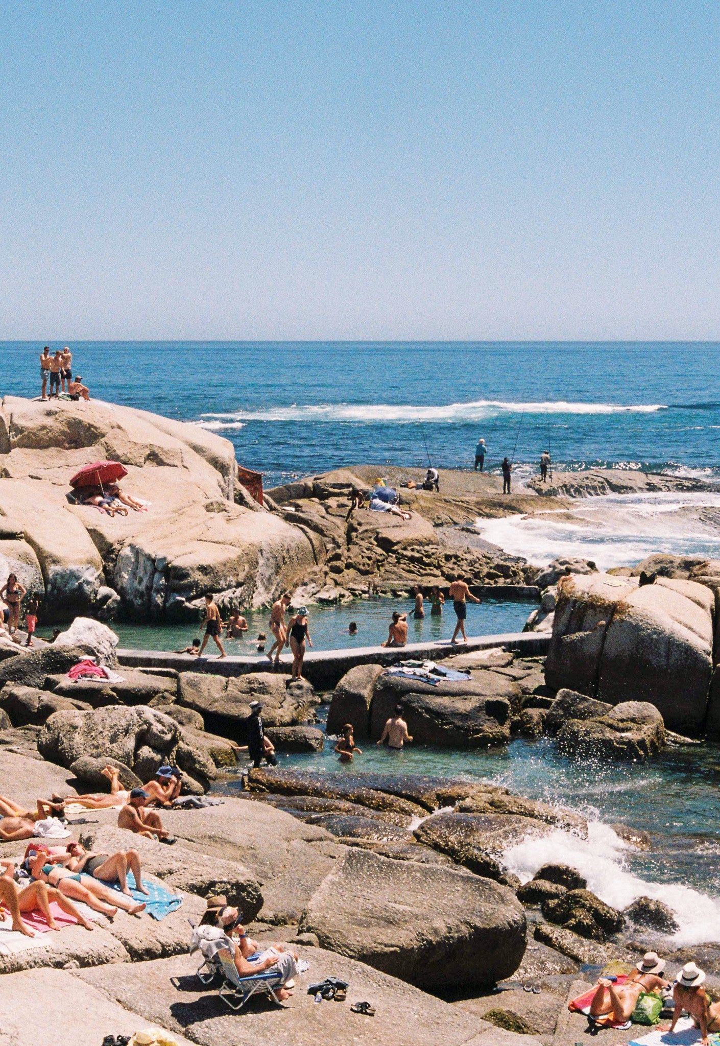 People enjoying the sun and cool water at a rocky beach.