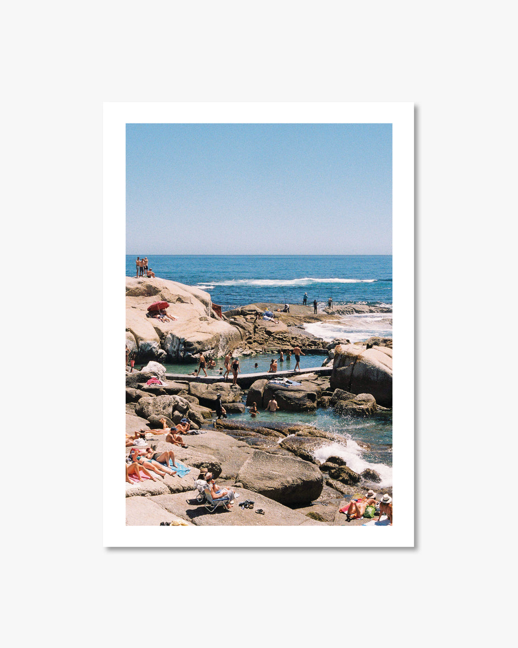 People enjoying a sunny day at a rocky beach with clear blue water and sky.