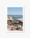People enjoying a sunny day at a rocky beach with clear blue water and sky.