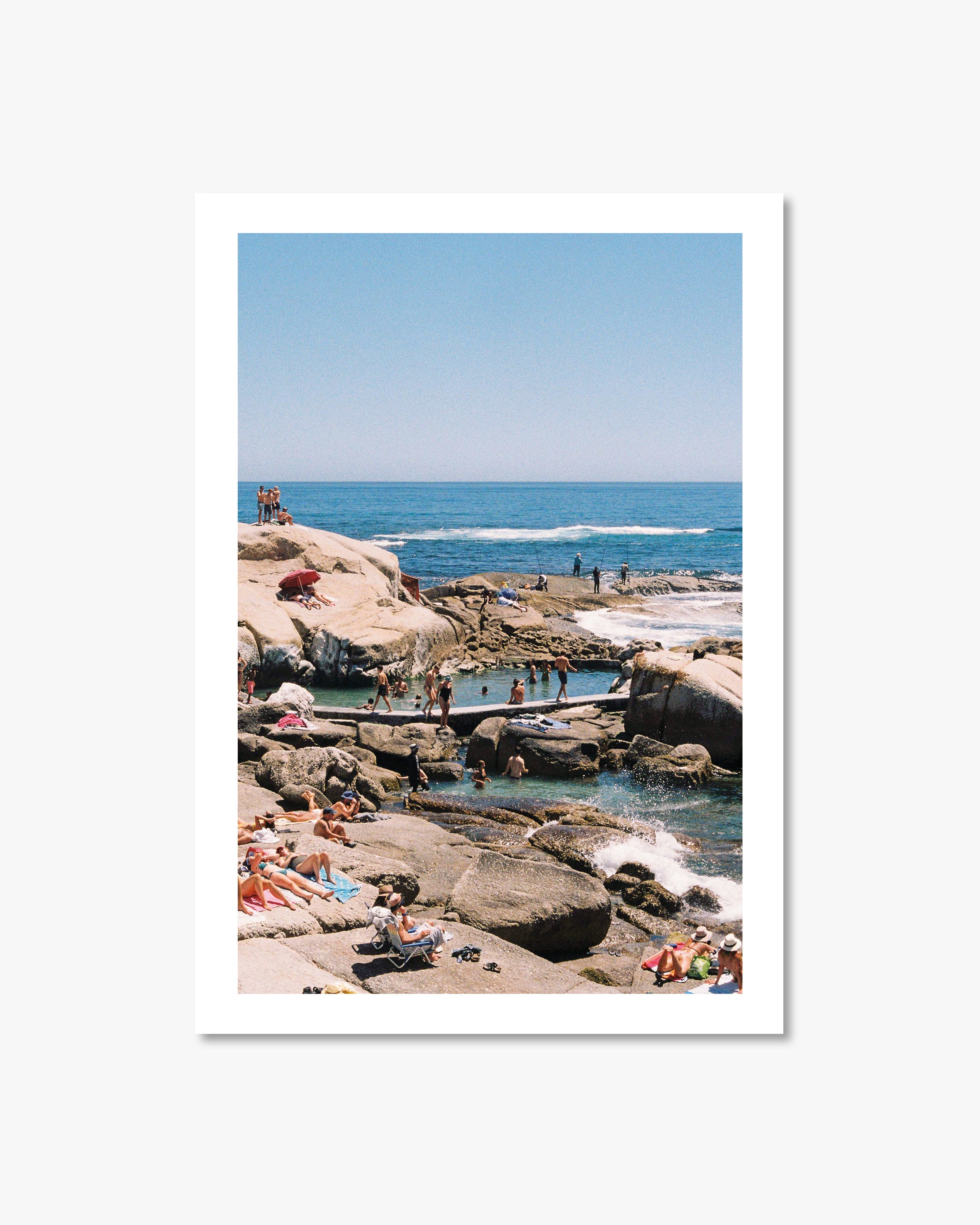 People enjoying a sunny day at a rocky beach with clear blue water and sky.