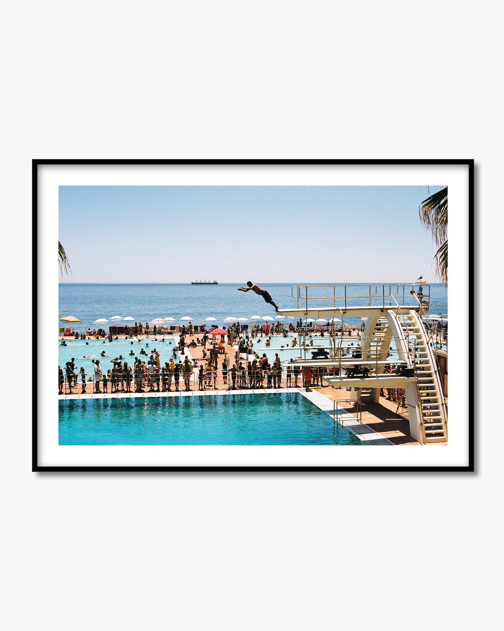 Framed photograph of a person diving into a pool with a beach and ocean view.