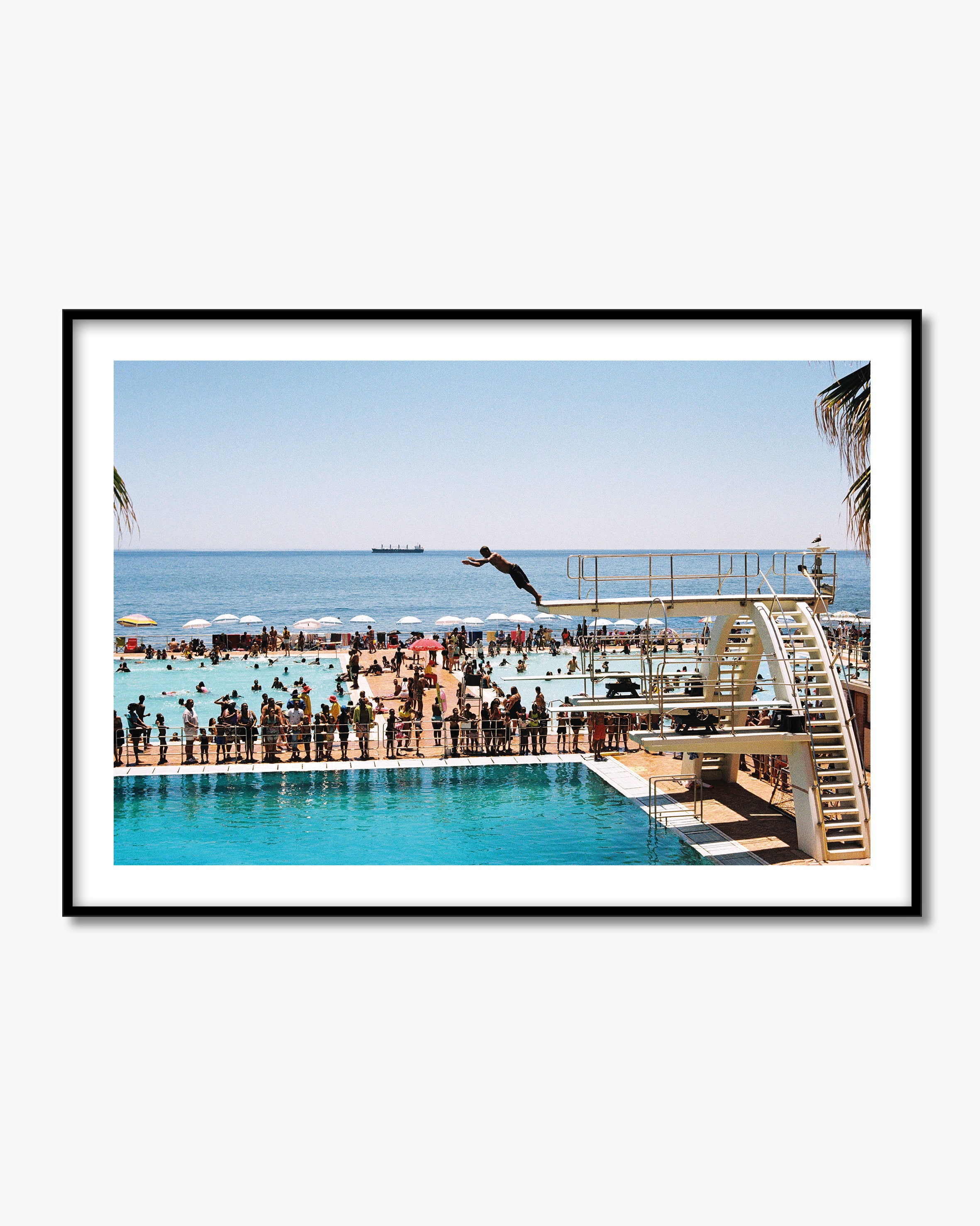 Framed photograph of a person diving into a pool with a beach and ocean view.