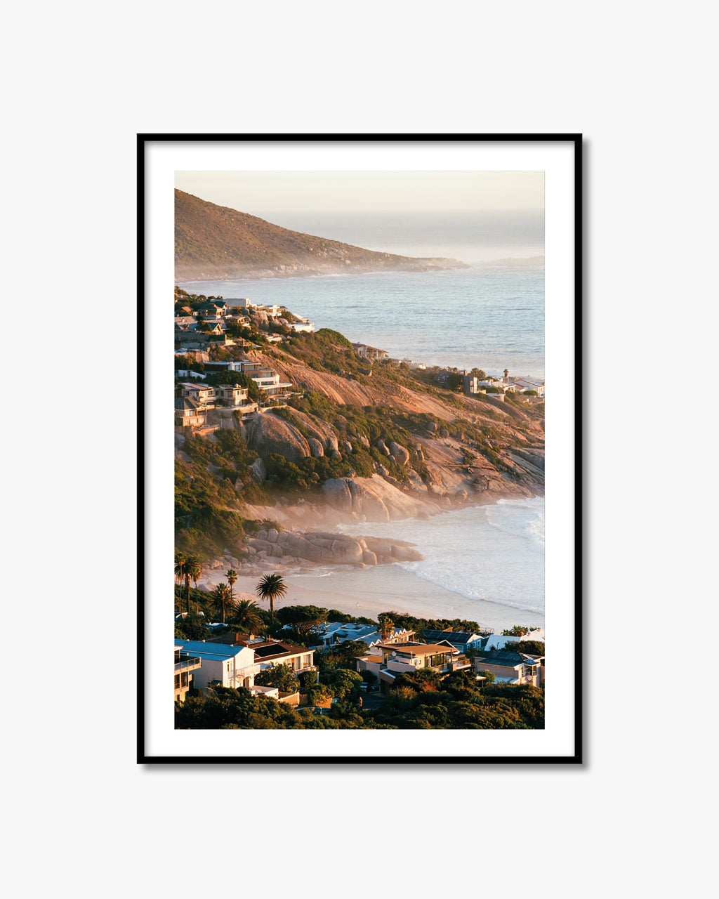 Framed artwork of a coastal landscape with houses and a mountain.