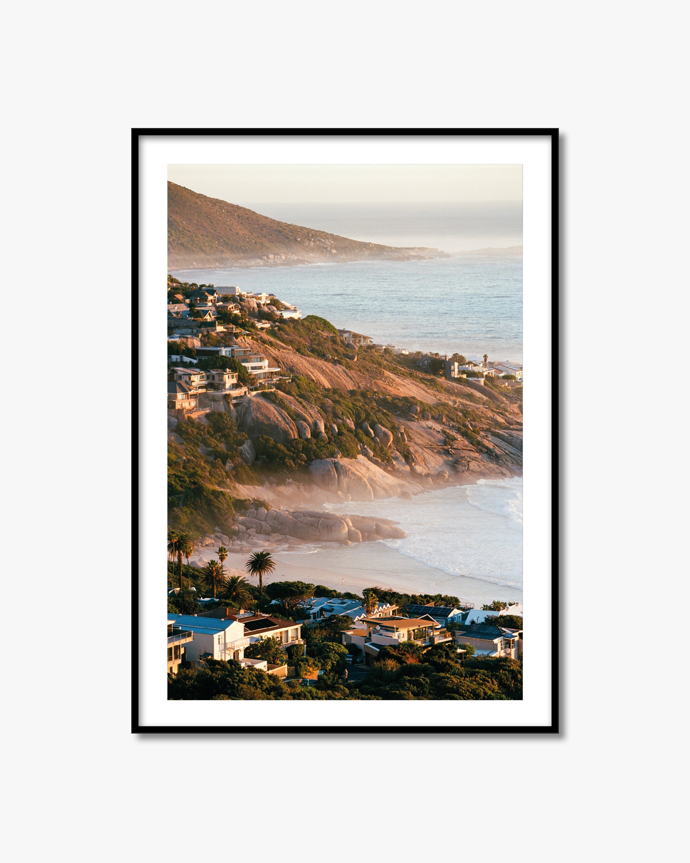 Framed artwork of a coastal landscape with houses and a mountain.
