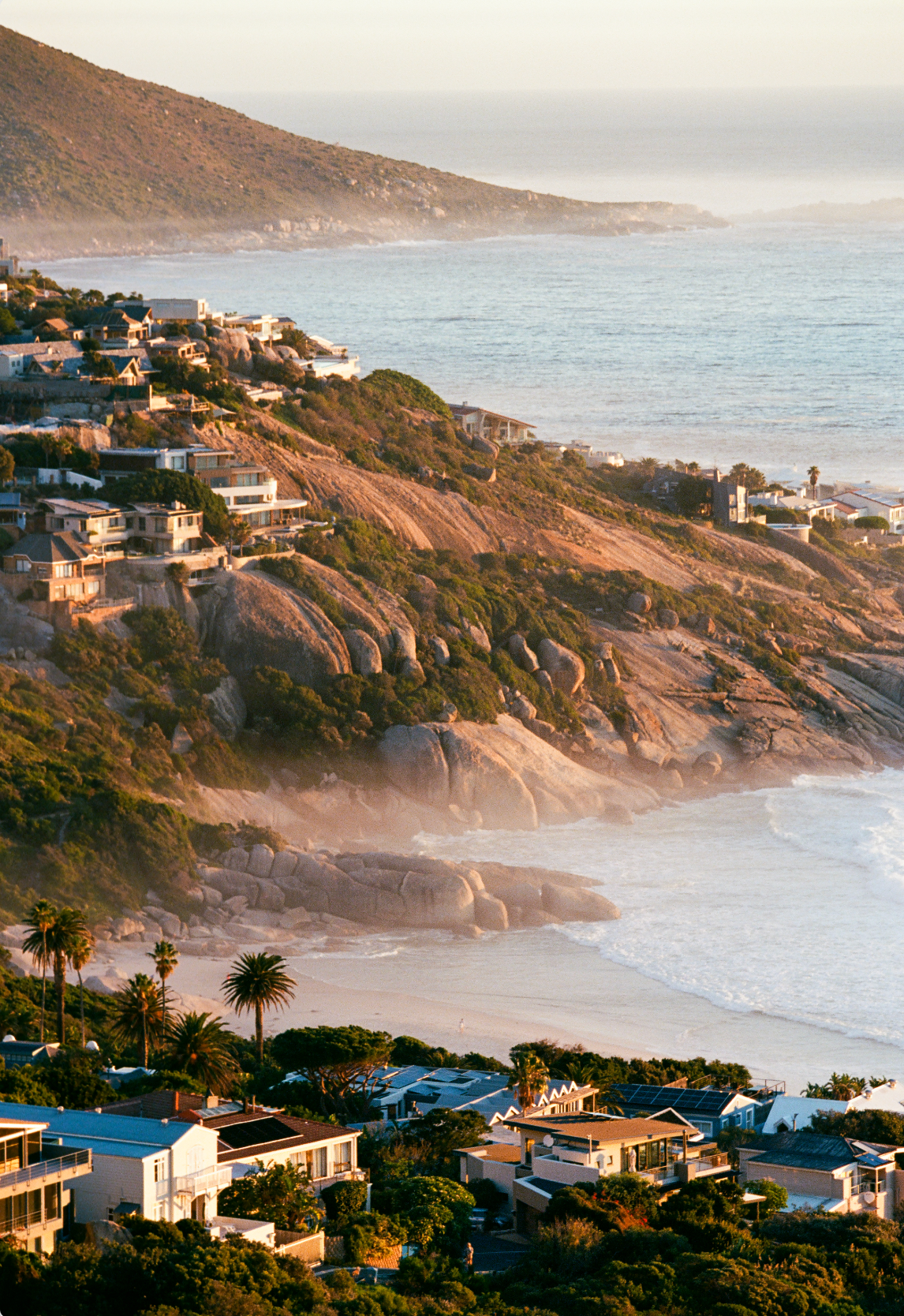Coastal landscape with houses on a hill overlooking the ocean.