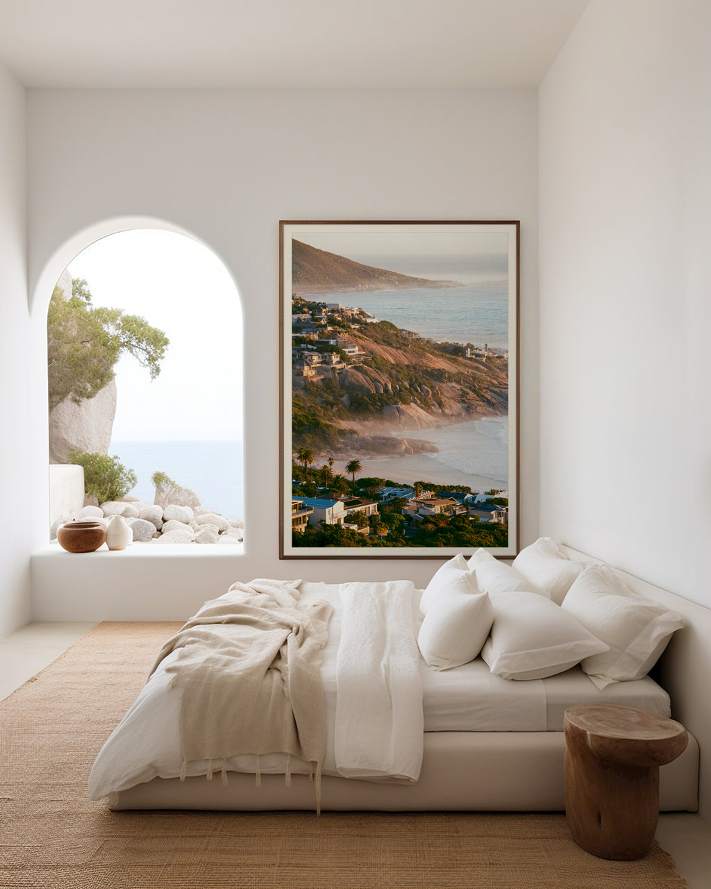Modern bedroom with a large bed, framed artwork of a coastal scene, and a window with an arched design.