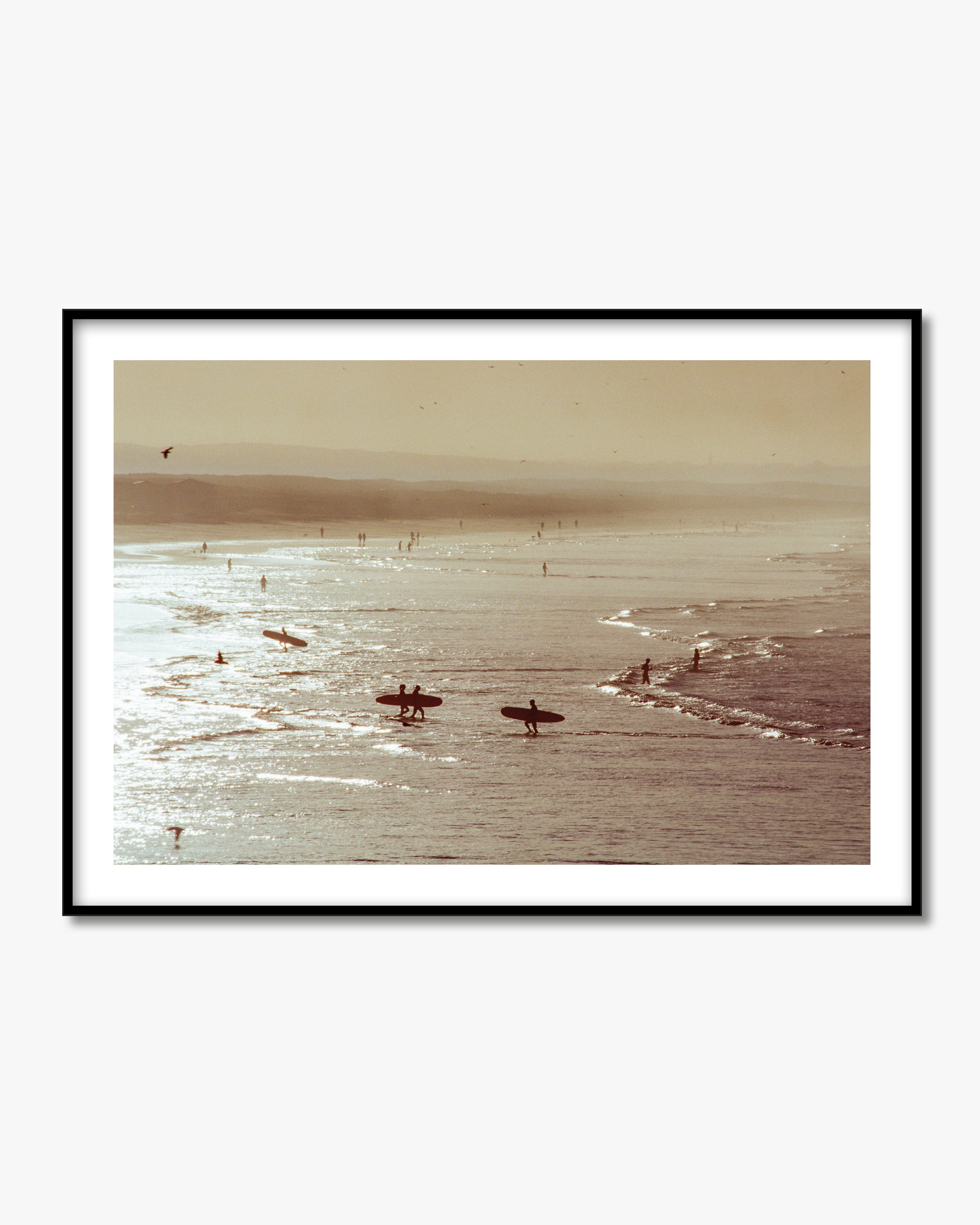 Framed artwork of a beach scene with people on surfboards and a horizon line.